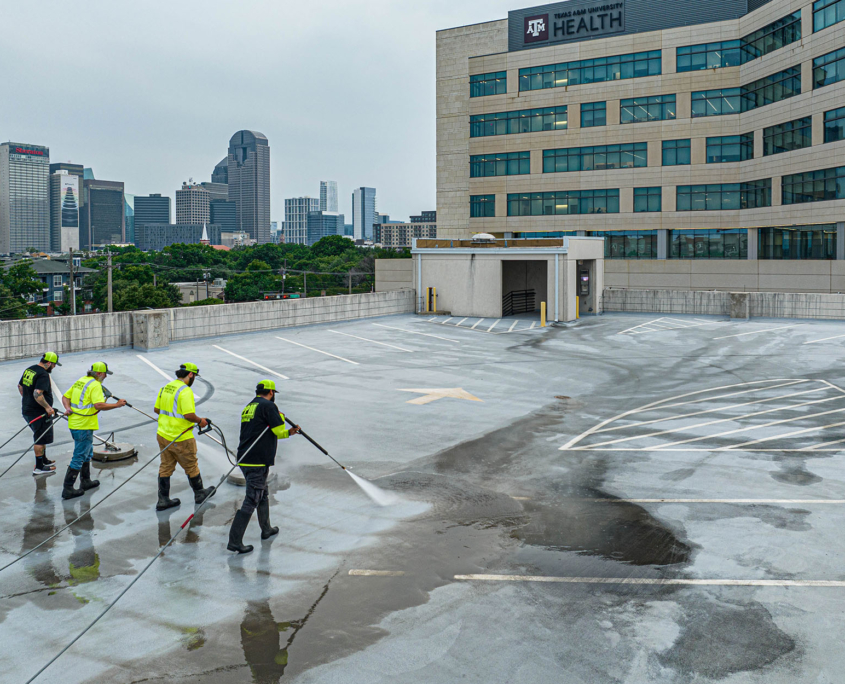 Aerial back view of four men powerwashing the top level of a parking garage